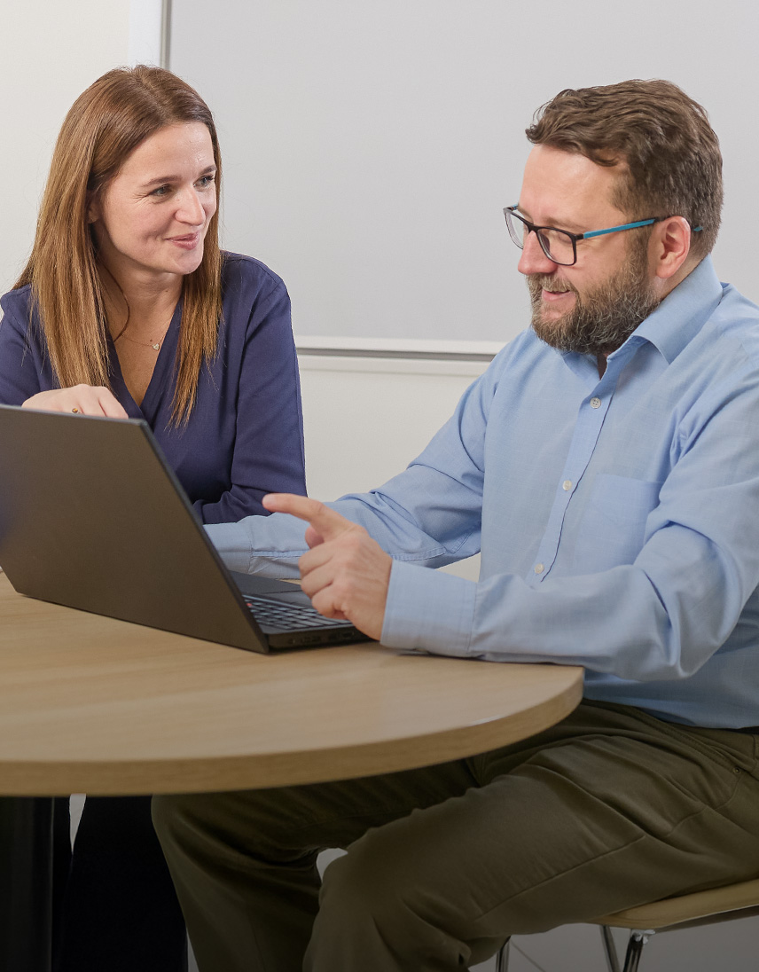 Zwei Personen arbeiten gemeinsam an einem Laptop in einem Büro.