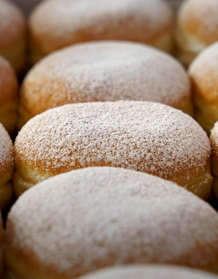 Mehrere Berliner mit Puderzucker bestäubt, dicht nebeneinander angeordnet.