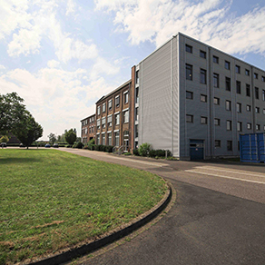 Mehrstöckiges Gebäude mit Backstein- und Metallfassade neben einer Straße und Grünfläche.