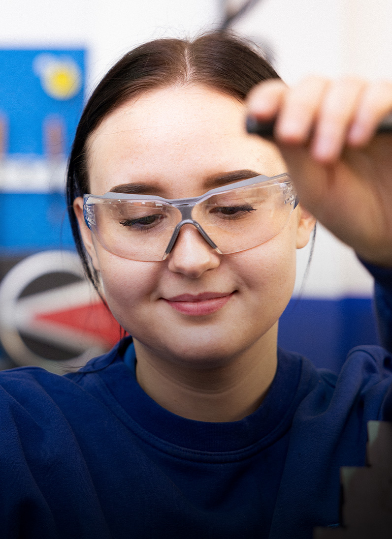 A woman wearing safety goggles is working on a machine