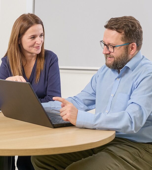 Zwei Personen arbeiten gemeinsam an einem Laptop in einem Büro.
