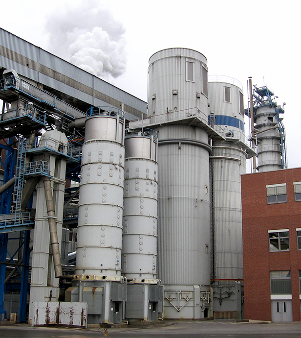 Industrieanlage mit Silos, Rohrleitungen und aufsteigendem Dampf.